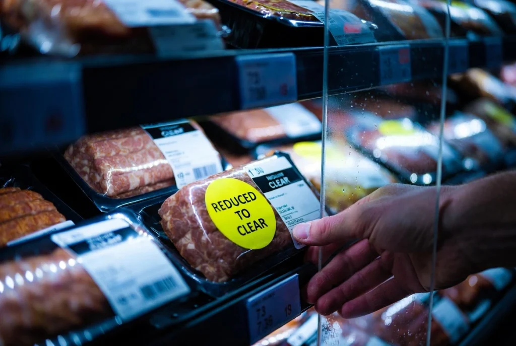 A close-up of a hand reaching for a food item with a bright yellow 'REDUCED' sticker in a UK supermarket.